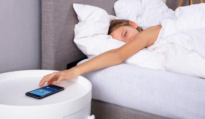 Girl,Lying,On,Bed,Snoozing,Alarm,On,Cellphone