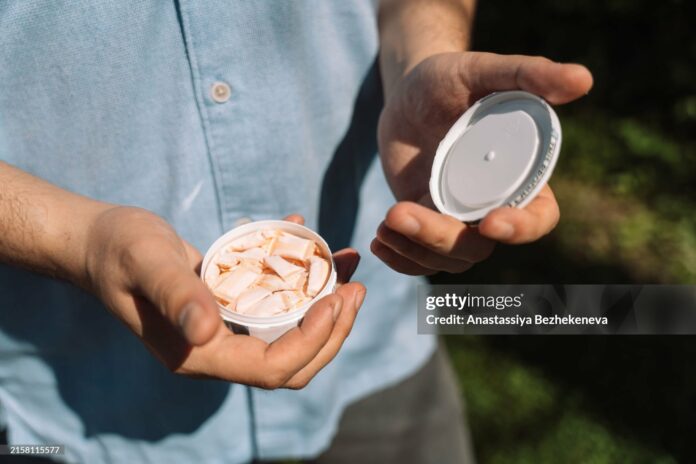 A man opens a plastic can of snus.